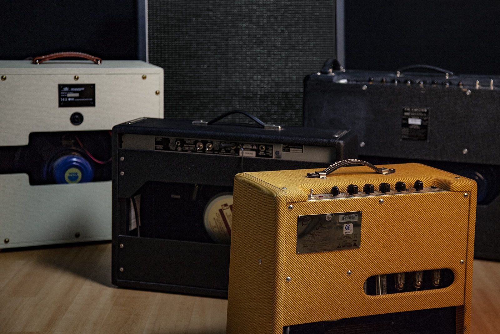 The back of several guitar combo amps, showing the back of their speakers.
