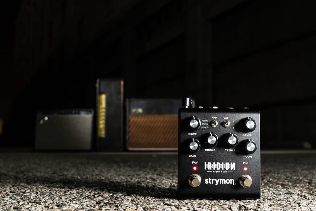 Strymon Iridium in dramatic lighting, with Fender, Marshall, and Vox amps propped up in the background