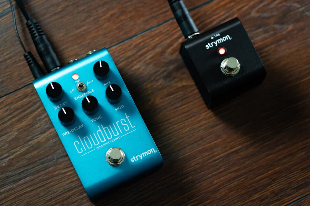 Strymon MiniSwitch connected to a Strymon Cloudburst ambient reverb pedal with a single TRS pedal against a dark wood backdrop