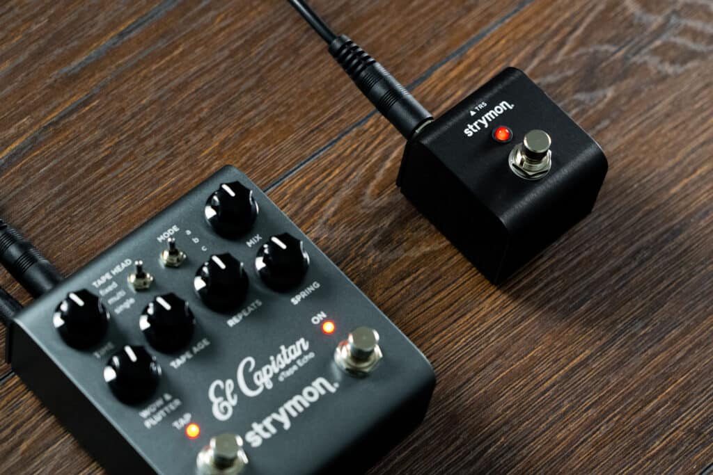 Strymon MiniSwitch connected to a Strymon El Capistan delay pedal with a single TRS pedal against a dark wood backdrop