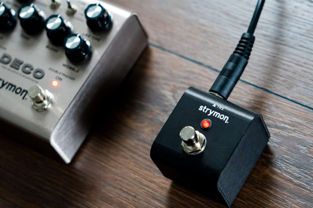 Strymon MiniSwitch connected to a Strymon Deco tape saturation and double tracker pedal with a single TRS pedal against a dark wood backdrop