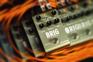 Strymon Brig with psychedelic visual effect resting on orange instrument cables.