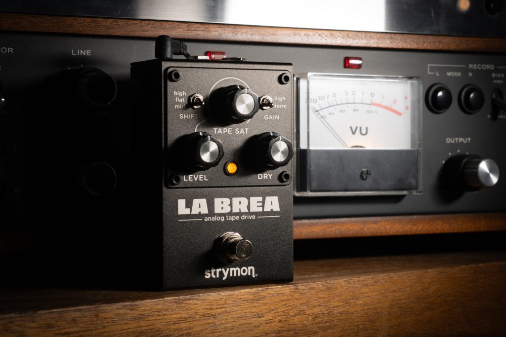 La Brea sitting on a wooden ledge in front of a vintage tape machine.