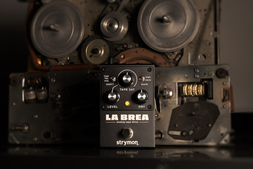 Strymon La Brea pedal sitting on a work bench in front of a disassembled tape machine.